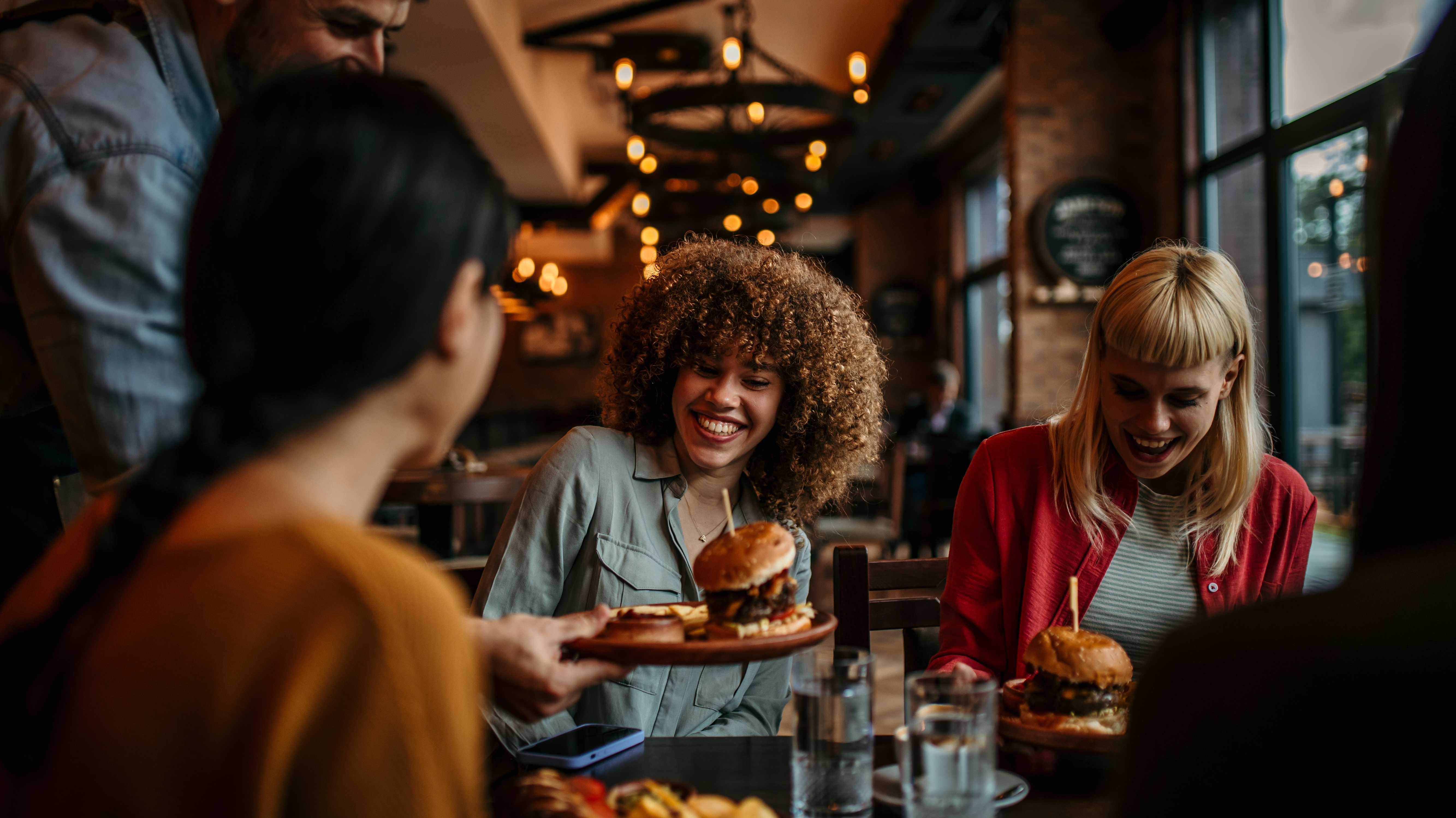 Friends smiling as burgers arrive at their restaurant table